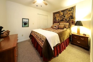 A bedroom with a bed, a nightstand, a dresser, a tapestry, a door, and a framed picture on the wall.