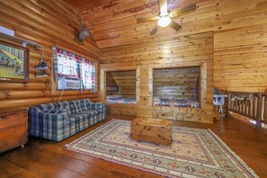 Ein Innenraum einer Blockhütte mit einem karoüberzogenen Sofa, einem Holztisch und einem Deckenventilator.