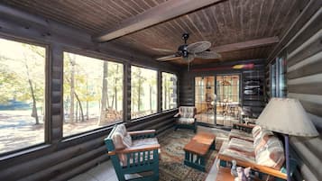 A log cabin interior with a large window, a ceiling fan, and a dining area with a table and chairs.