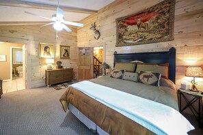 A bedroom with a bed, a ceiling fan, a wooden headboard, a painting, and a door.