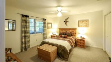 A bedroom with a bed, two bedside tables, a nightstand, a window with curtains, a ceiling fan, and a wall-mounted bird decoration.