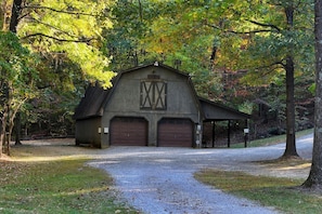 A barn with two large garage doors, a covered area, and a gravel driveway leading to it.