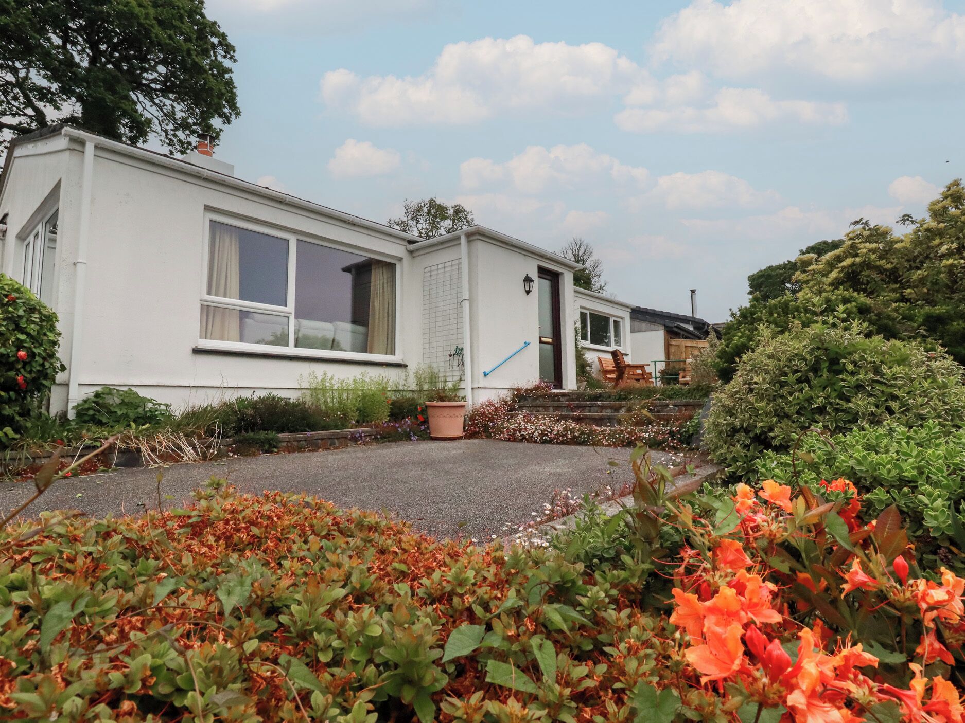 A white mobile home with a front porch, a small garden with various plants, and a clear sky.