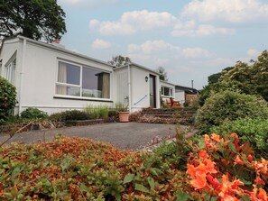A white mobile home with a front porch, a small garden with various plants, and a clear sky. - 7 Chycoose Parc (Truro)