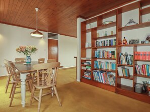 A dining area with a wooden table and chairs, a vase of flowers, and a bookshelf filled with books and decorative items. - 7 Chycoose Parc (Truro)