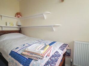 Un lit bien fait, avec une couverture matelassée, une table de chevet avec une lampe et une étagère sur laquelle sont posés un jouet en peluche et un livre.