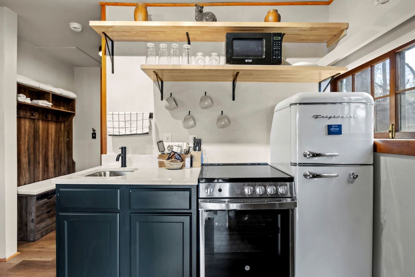 A kitchen with a built-in stove, a refrigerator, and a microwave on a wooden shelf.