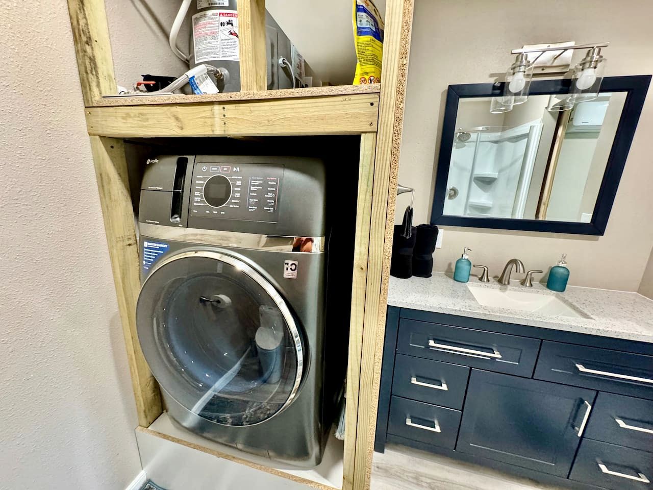 Ein kleiner Waschbereich mit Waschmaschine, Spiegel und Waschbecken mit Arbeitsplatte.