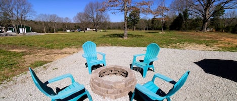 A gravel area with four blue Adirondack chairs arranged around a central fire pit.