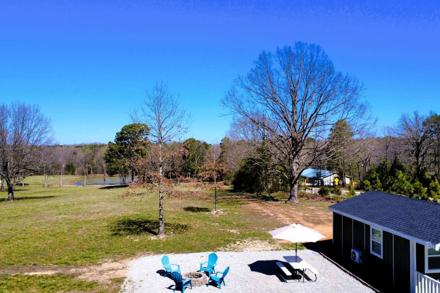 A backyard with a gravel patio, two blue Adirondack chairs, a small table, and a shed.