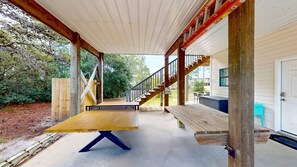 Ein überdachter Außenbereich mit Holztisch und Bank, einer Treppe und Blick auf ein Haus.