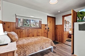 Une chambre à coucher avec un lit, des murs en bois, une fenêtre et une porte donnant sur une autre pièce.