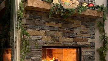 Une cheminée en pierre avec un feu de bois, un tableau encadré et des décorations de saison.