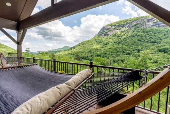 A hammock on a balcony with a view of a forested mountain.