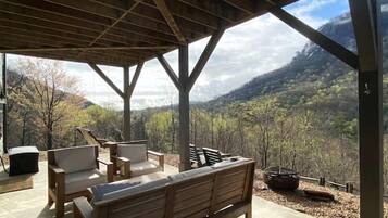 A covered outdoor seating area with wooden furniture and a view of a mountainous landscape.