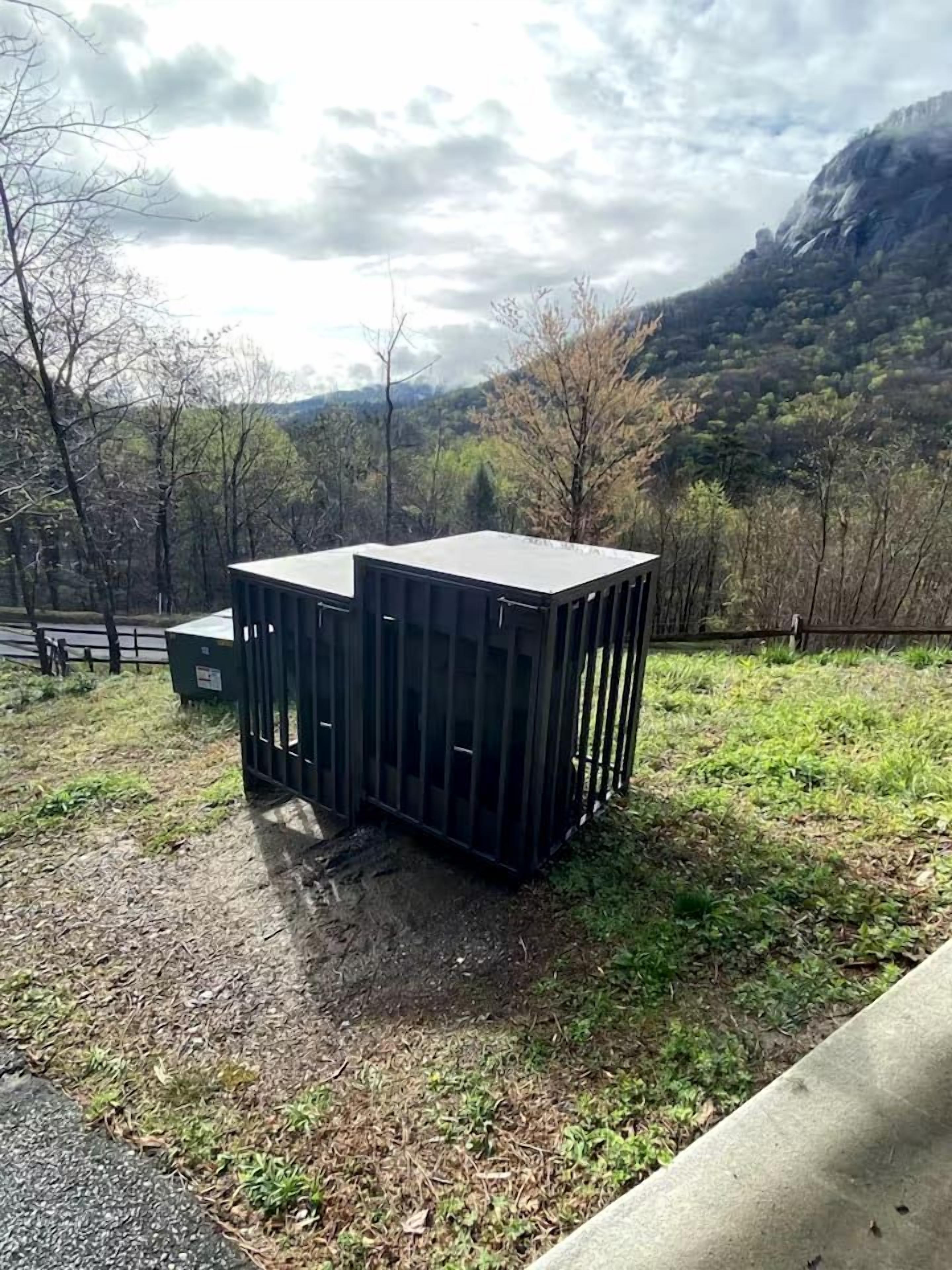 Due contenitori di grandi dimensioni e scuri in un ambiente esterno, con montagne sullo sfondo.
