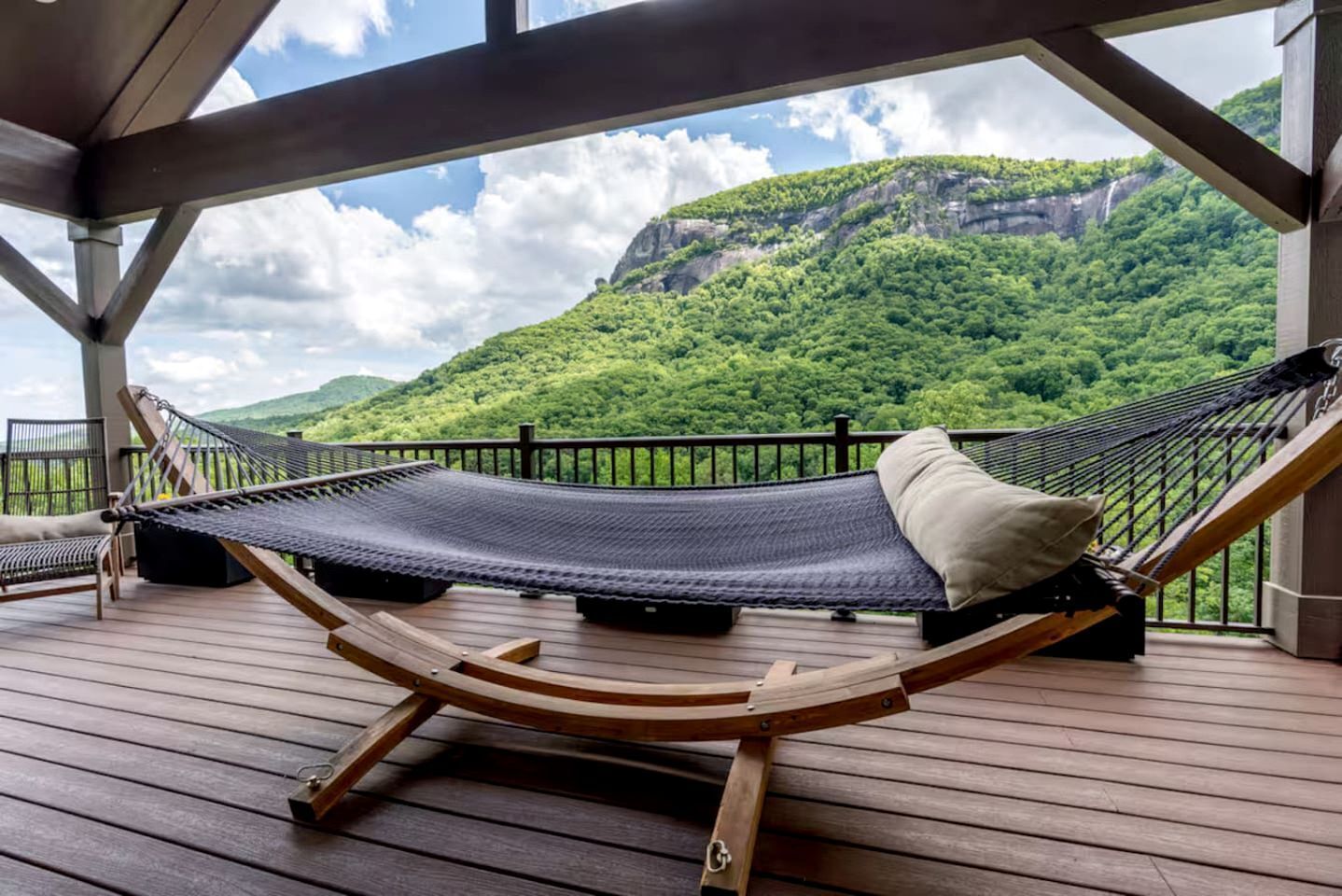 A hammock on a wooden deck with a view of a green mountain.