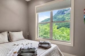 Ein Schlafzimmer mit einem großen Fenster, einem Bett mit einer Steudecke, Kissen und einem Stapel gefalteter Handtücher.
