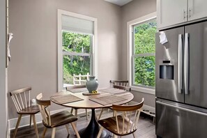 A modern kitchen with a large stainless steel refrigerator, a dining table with four chairs, and two windows offering a view of greenery. - Mountain Hideaway with Waterfall Views & Relaxing Hammocks in Chimney Rock, North Carolina (Chimney Rock)