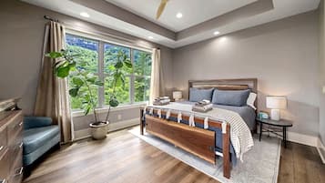 Ein Schlafzimmer mit Bett, Nachttischen, einer Bank, einem Fenster mit Vorhängen, einem Deckenventilator und einer Topfpflanze.