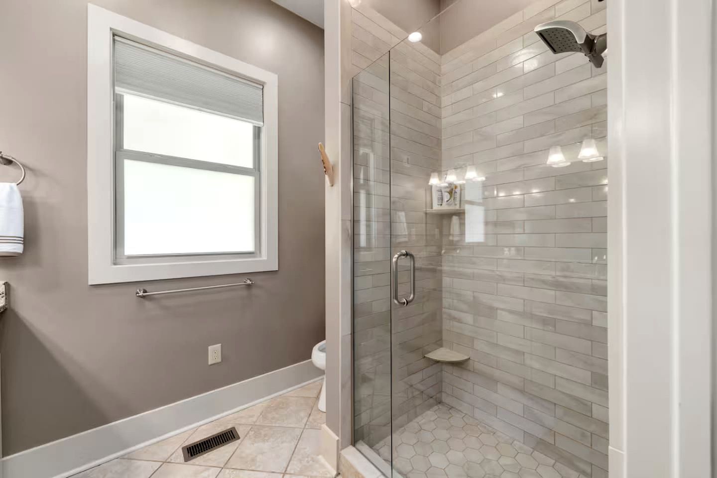 A modern bathroom with a glass-enclosed shower, a window, and a towel rack.