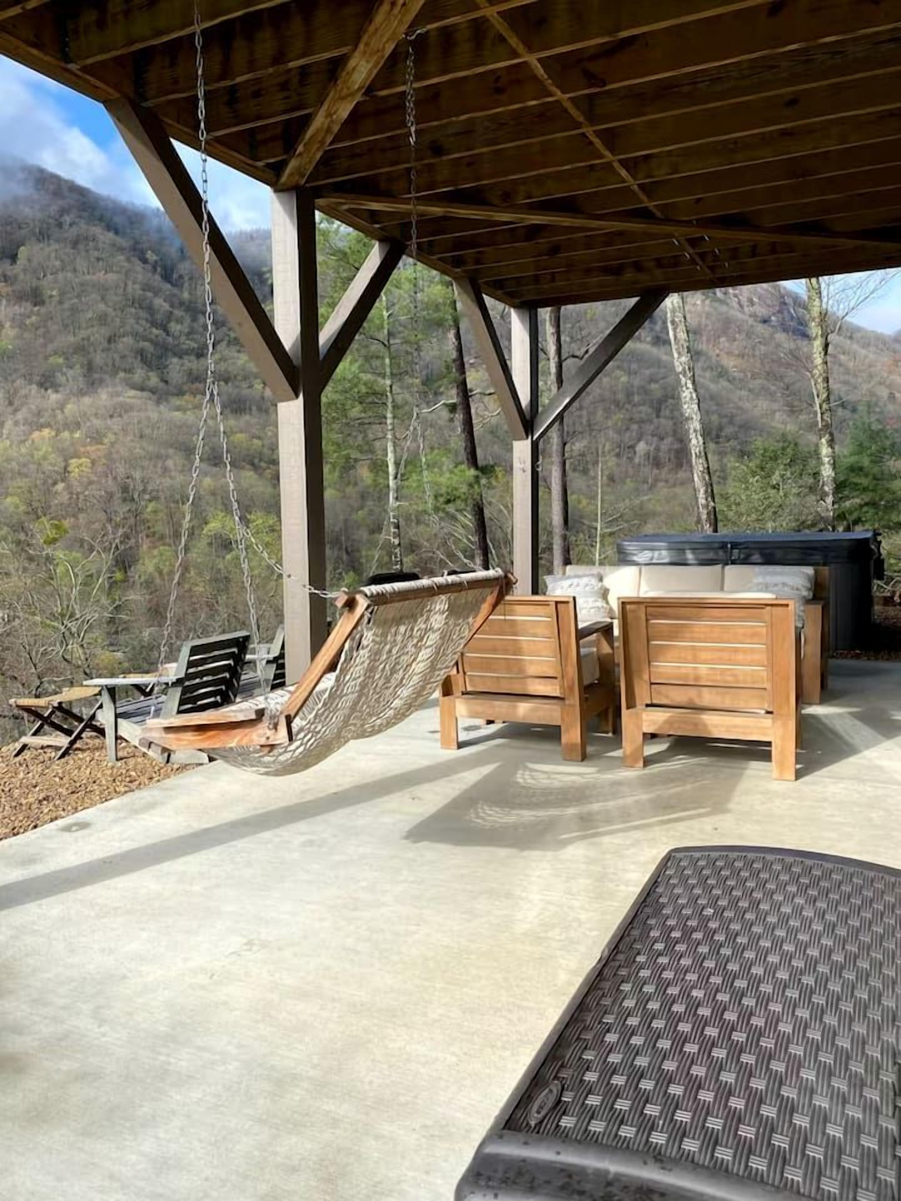 Un espacio de estar al aire libre cubierto con una hamaca, sillas de madera y una mesa.