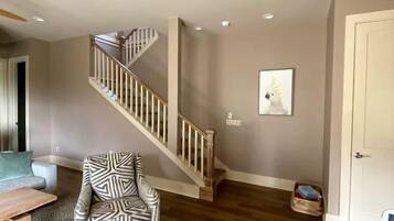 A spacious living area with a wooden staircase, a patterned armchair, and a ceiling fan.