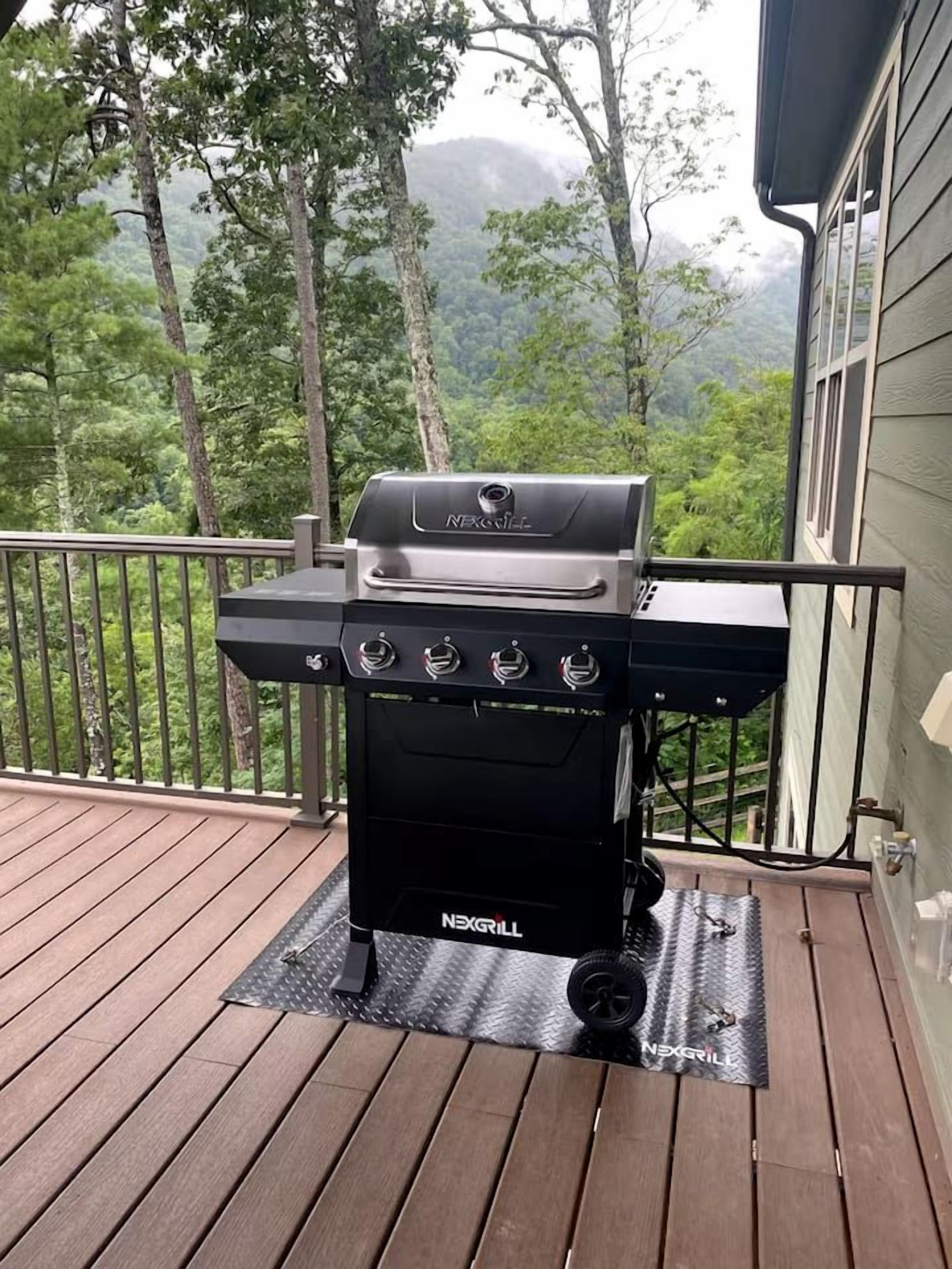 Een NEXGRILL barbecue op een houten terras, met uitzicht op bomen en bergen.