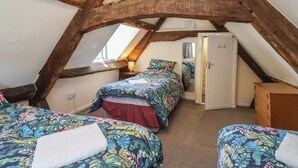 An attic bedroom with exposed wooden beams, two beds with floral bedding, a bedside lamp, and a walk-in closet. - Walk House (Gloucester)