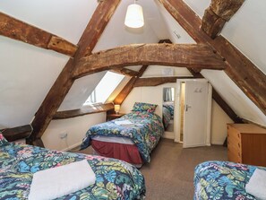 An attic bedroom with exposed wooden beams, two beds with floral bedding, a bedside lamp, and a walk-in closet. - Walk House (Gloucester)