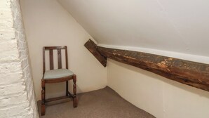 A corner of a room with a wooden chair, white walls, and a sloped ceiling. - Walk House (Gloucester)