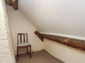 A corner of a room with a wooden chair, white walls, and a sloped ceiling. - Walk House (Gloucester)