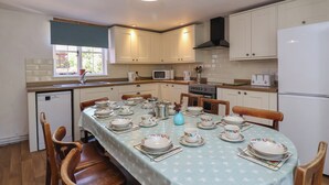 A kitchen with white cabinets, a dining table set with plates and cups, a microwave, and a stove. - Walk House (Gloucester)