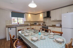 A kitchen with white cabinets, a dining table set with plates and cups, a microwave, and a stove. - Walk House (Gloucester)