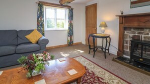 A living room with a sofa, a table with a vase of flowers, a lamp, a fireplace, and a window with curtains. - Walk House (Gloucester)