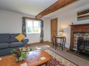 A living room with a sofa, a table with a vase of flowers, a lamp, a fireplace, and a window with curtains. - Walk House (Gloucester)