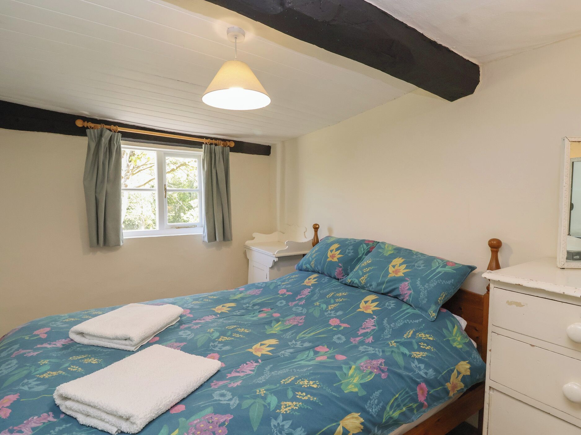 Une chambre à coucher avec un lit, une fenêtre avec des rideaux, une table de chevet et une commode.