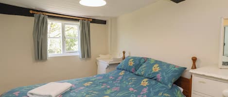 A bedroom with a bed, a window with curtains, a bedside table, and a nightstand.