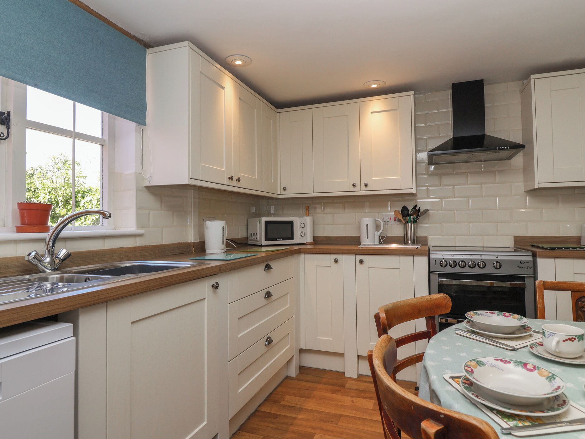 A kitchen with white cabinets, a stainless steel sink, a microwave, a stove, and a window with a view of greenery.