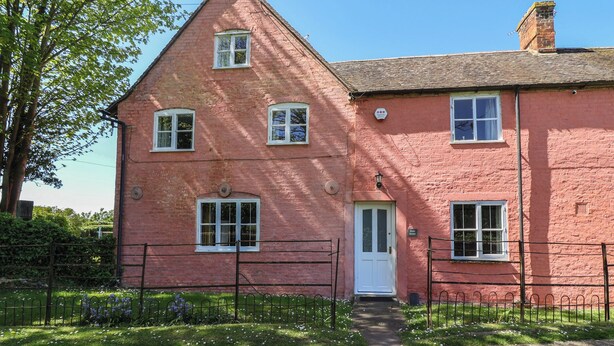 A red brick building with a white door, multiple windows, and a small garden area with a metal fence. - Walk House (Gloucester)