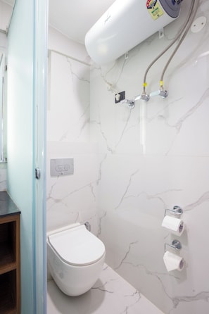 Et badeværelse med toilet, bruser og vandvarmer.