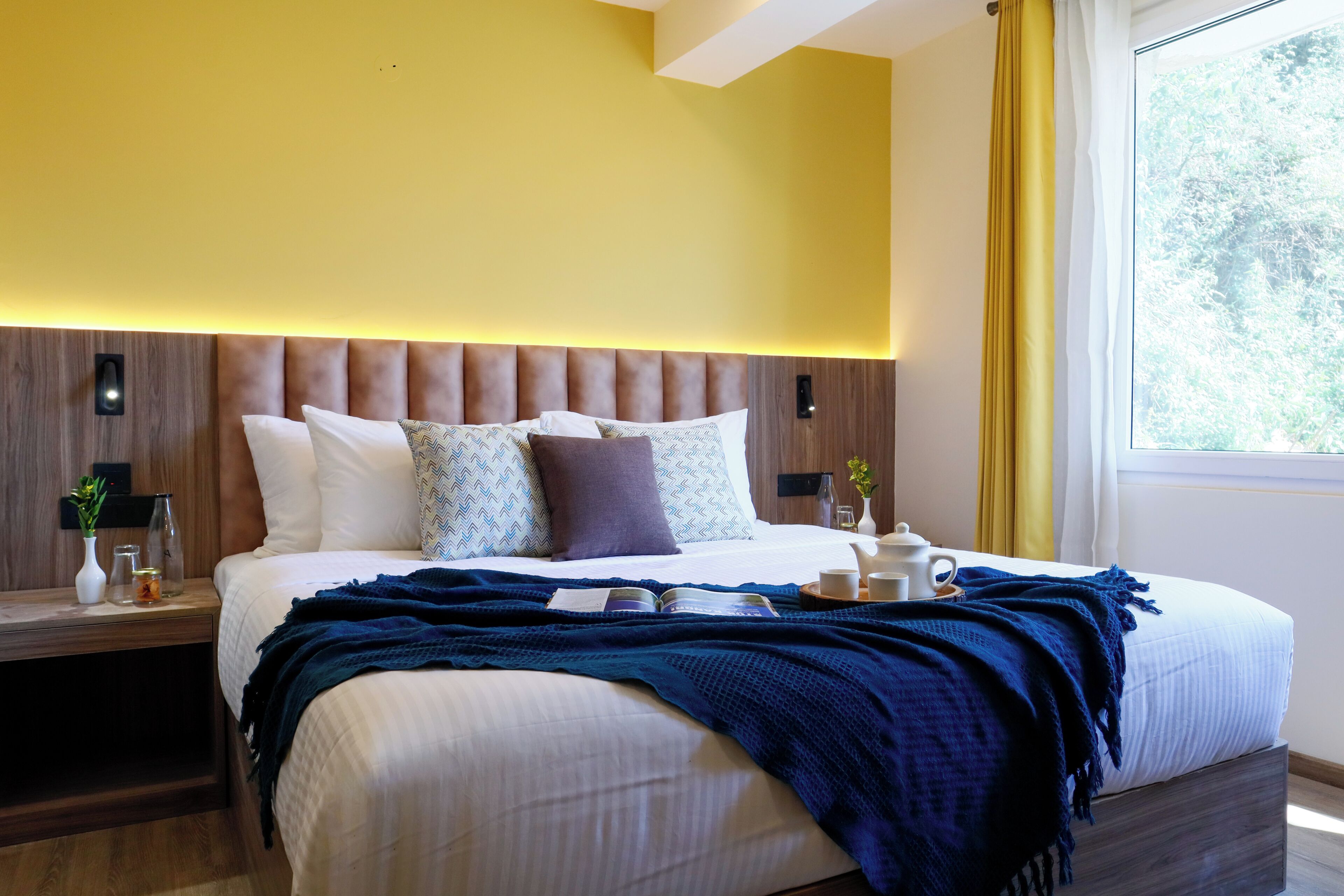 A modern hotel room with a large bed, bedside tables, a nightstand, and a window with curtains.