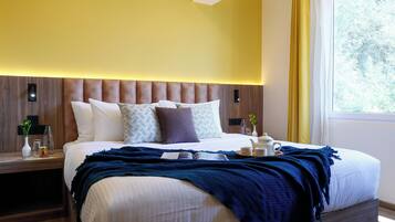 A modern hotel room with a large bed, bedside tables, a nightstand, and a window with curtains.