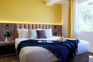 A modern hotel room with a large bed, bedside tables, a nightstand, a window with curtains, and a view of trees. - Alaya Stays Baljees Melville Divine 1BHK (Shimla)