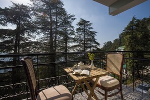 Ein Balkon mit Tisch, Stühlen, einem Buch, einer Teekanne und einem Blumenstrauß in einer Vase.