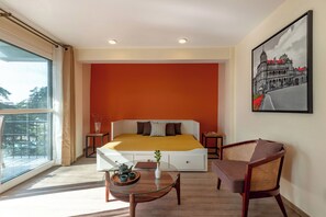 A modern hotel room with a large bed, a glass table with tea set, a wicker chair, and a cityscape painting. - Alaya Stays Baljees Melville Divine 1BHK (Shimla)