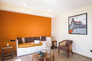 Ein Zimmer mit einem weißen Sofa, einem Glastisch, einem Korbstuhl und einem gerahmten Bild an der Wand.