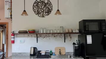 Uma cozinha com micro-ondas, chaleira e diversos utensílios sobre o balcão.