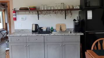 Una cocina con armarios grises, un refrigerador negro y una silla de madera.