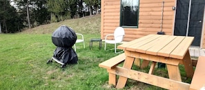 En træhytte med et picnicbord og stole, en overdækket grill og en dør med et vindue.